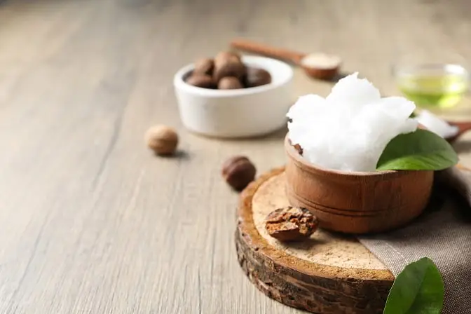 Bodegón con manteca de karité en un cuenco de madera y nueces de karité, representando su textura ideal para nutrir y suavizar la piel.
